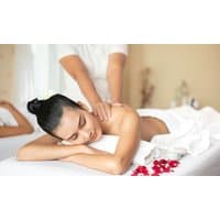 Woman receiving a back massage on a white towel, surrounded by red rose petals, in a serene spa setting.