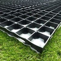 Black grid-patterned plastic shed base kit on grass, featuring interlocking square cells for stability and drainage.