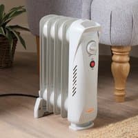 White mini oil-filled radiator with control dial and red indicator light, placed on wooden floor near a chair.