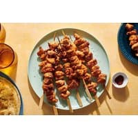 Turkish dining set with skewered meat on a blue plate, small sauce dish, and glasses on a yellow table.