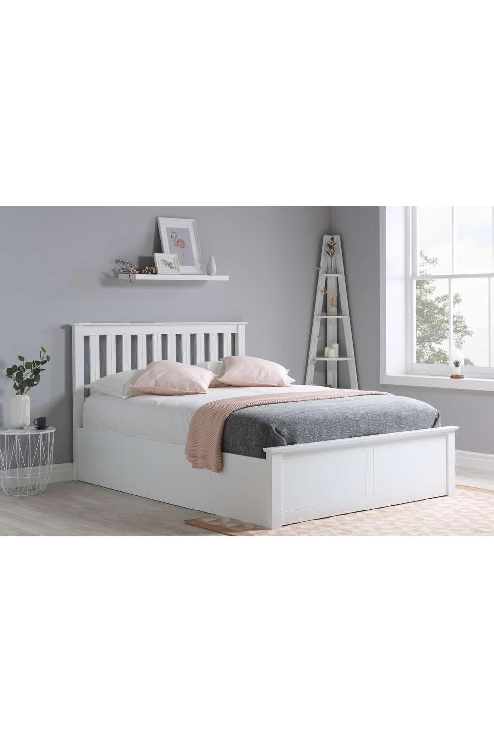 Birlea Solid Wood Ottoman Storage Bed Frame in white with a gas lift mechanism, featuring a slatted headboard and spacious under-bed storage, styled with a gray blanket and pink throw.