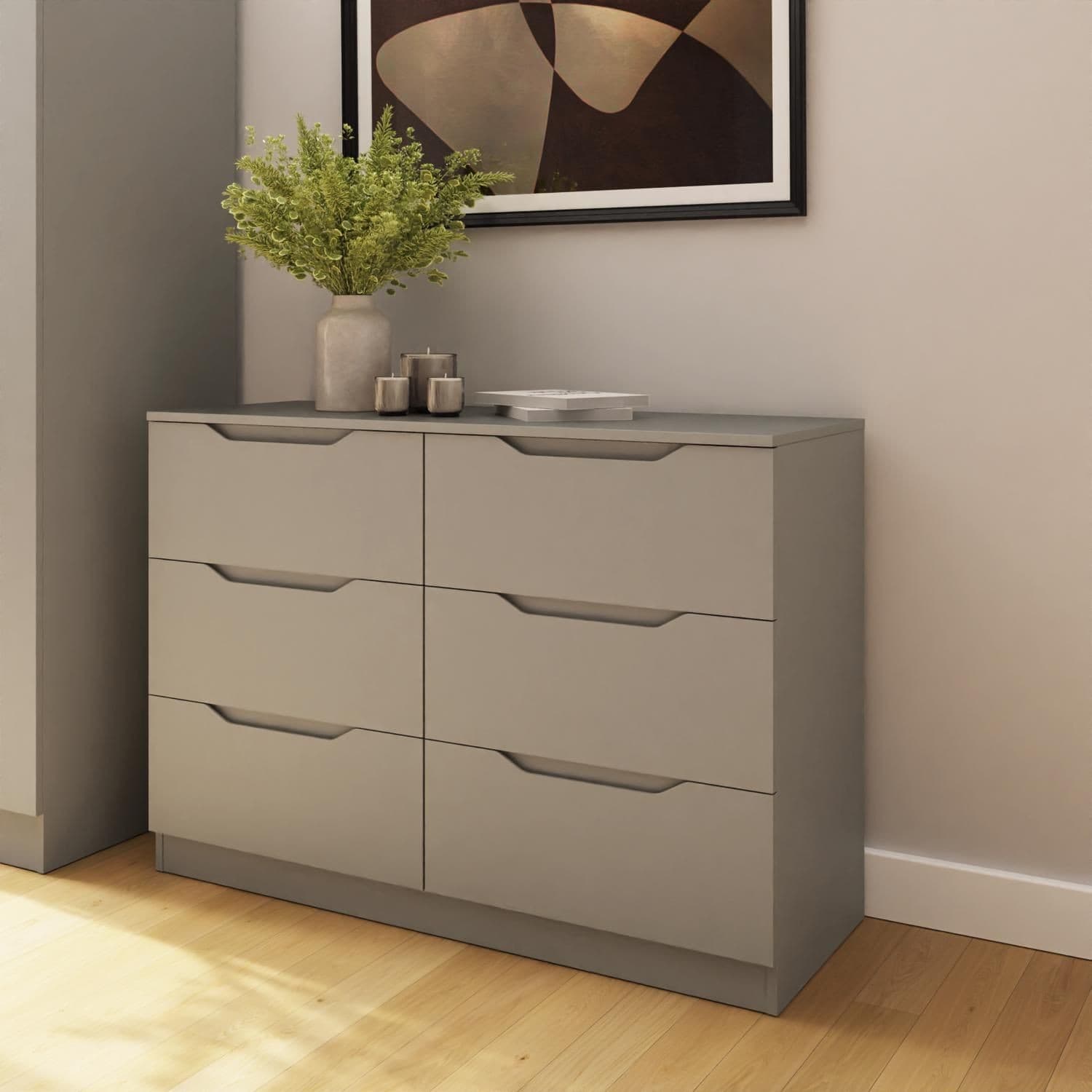 Modern wide chest of drawers in beige with six smooth, handle-less drawers, featuring a sleek design and a minimalist aesthetic, placed against a light wall with decorative plants.