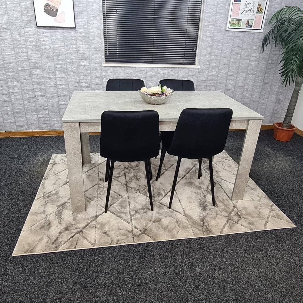 Grey KOSY KOALA dining table with four black upholstered chairs, set on a patterned rug, surrounded by a minimalist room with decorative wall art and a potted plant.
