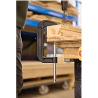 Black Draper heavy-duty G-clamp, 150mm, securing wooden planks on a workbench, with a metal screw mechanism.