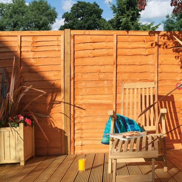Rowlinson Lap Panels in a warm, dipped wood finish, featuring a sturdy design with horizontal slats, set against a garden backdrop with greenery and a wooden chair.