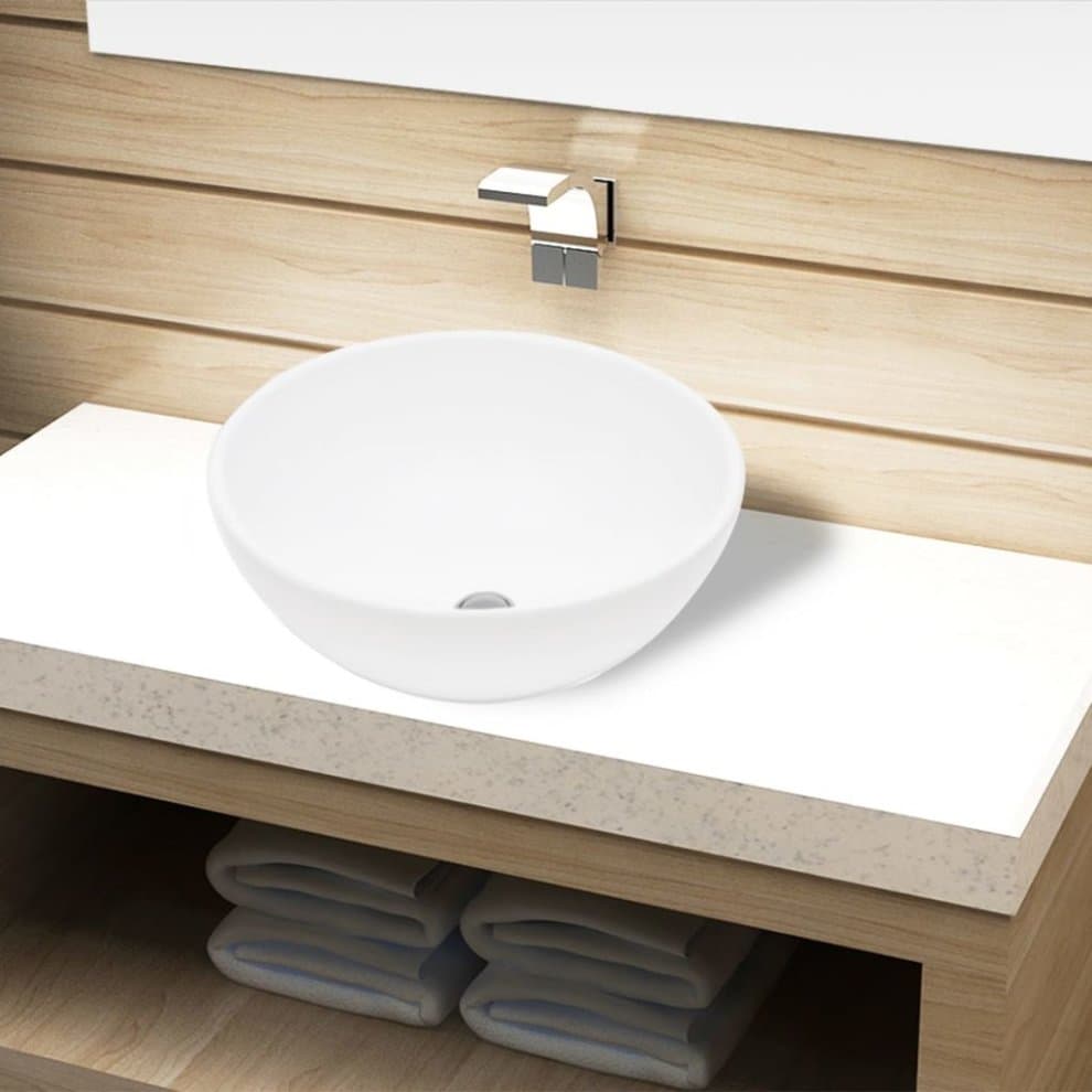 Round white ceramic bathroom sink basin with a smooth finish, set on a light wooden countertop, featuring a modern faucet above and neatly stacked towels below.