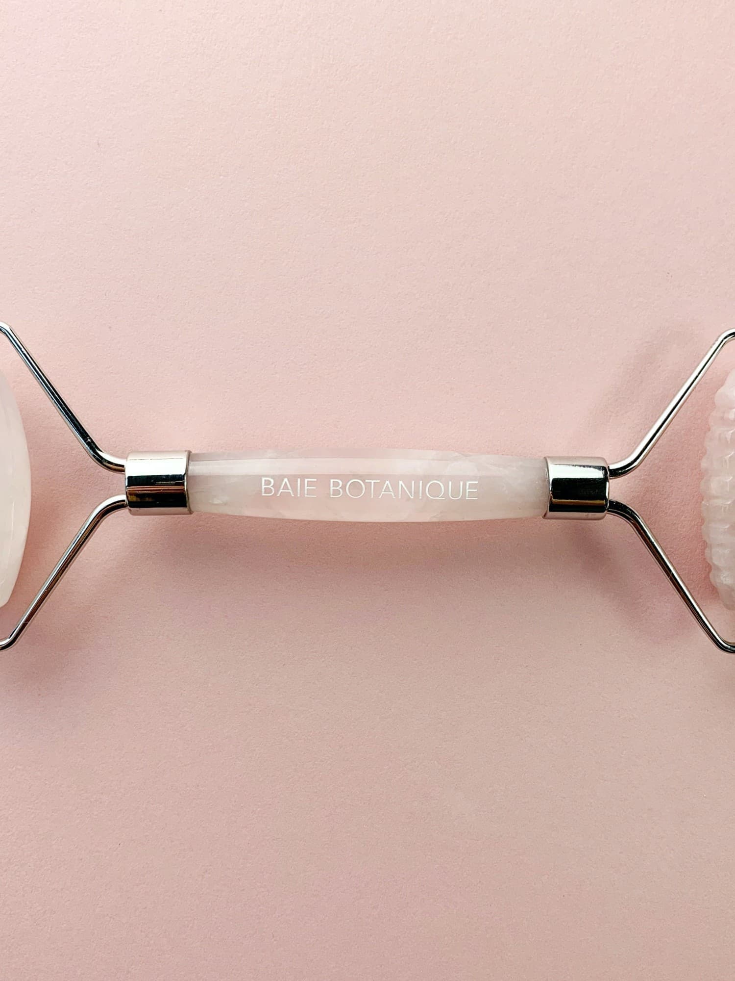 Rose quartz gua sha tool with a smooth, pale pink surface, featuring a silver metal handle and the text "BAIE BOTANIQUE" engraved on the center.