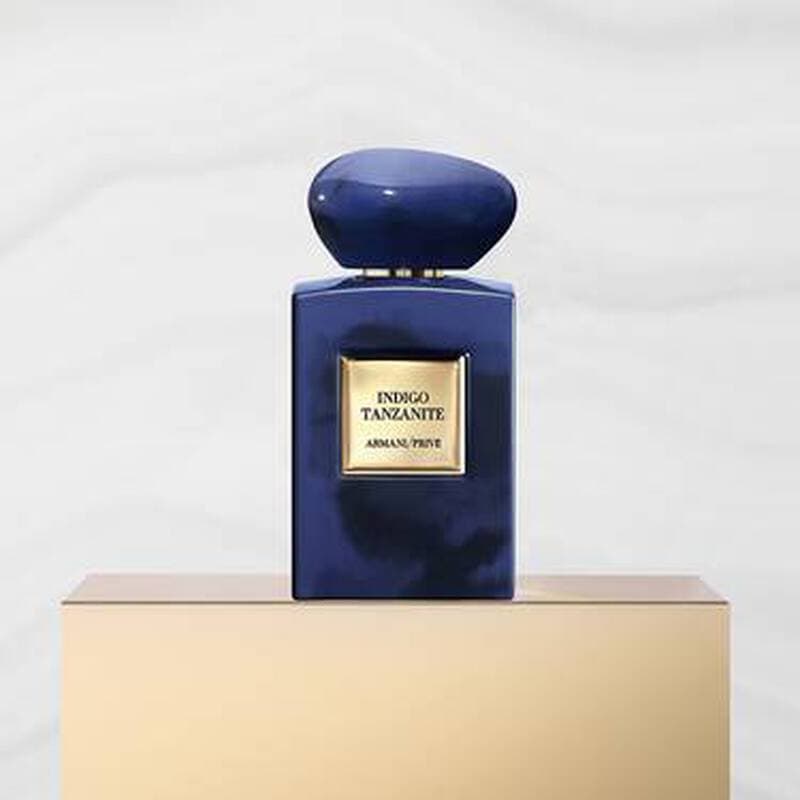 Deep blue glass bottle with a smooth, rounded cap, featuring a gold label that reads "Indigo Tanzanite" by Armani Beauty, set against a light marble background.