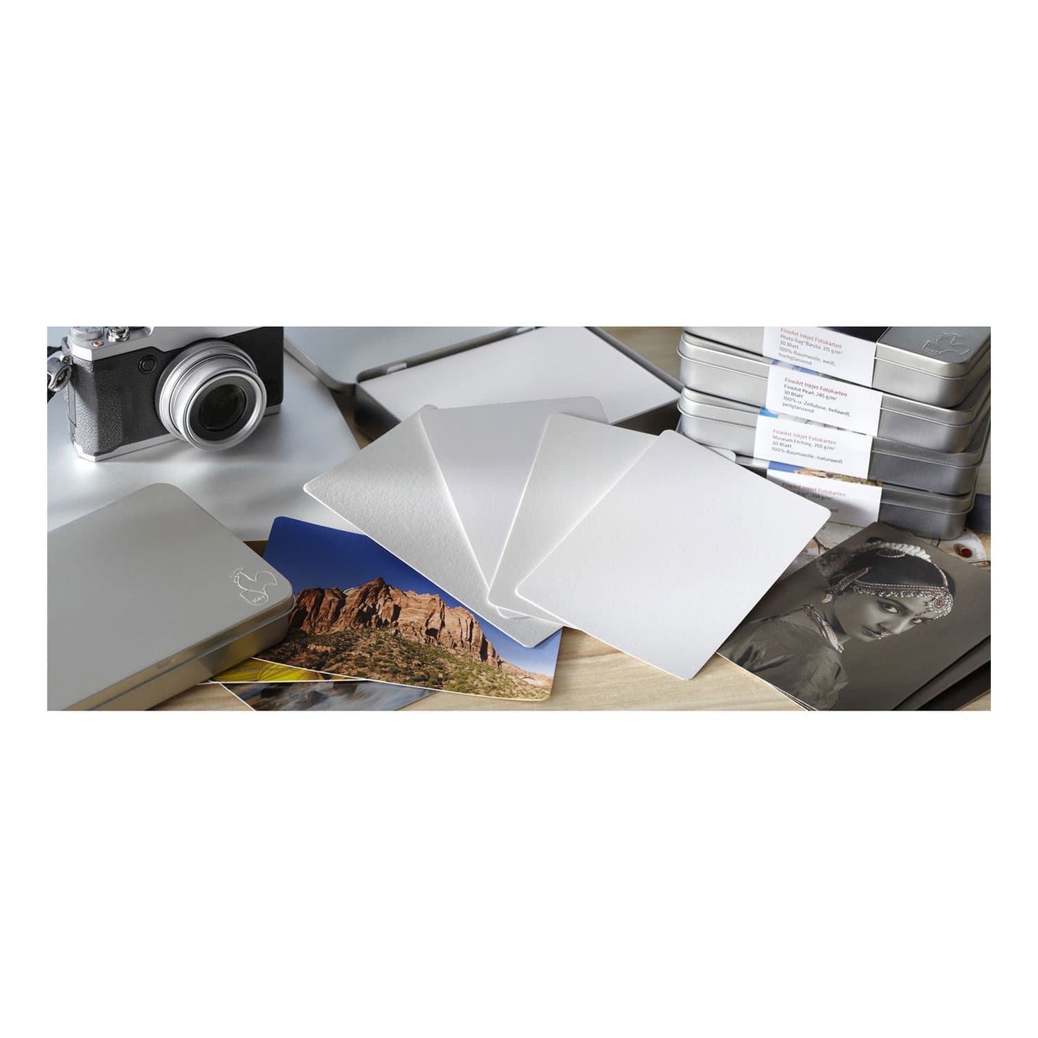 Hahnemühle Pho Rag Ultra Smooth paper sheets in a sleek silver tin, featuring smooth, white texture, ideal for high-quality prints, alongside a camera and various printed photos.