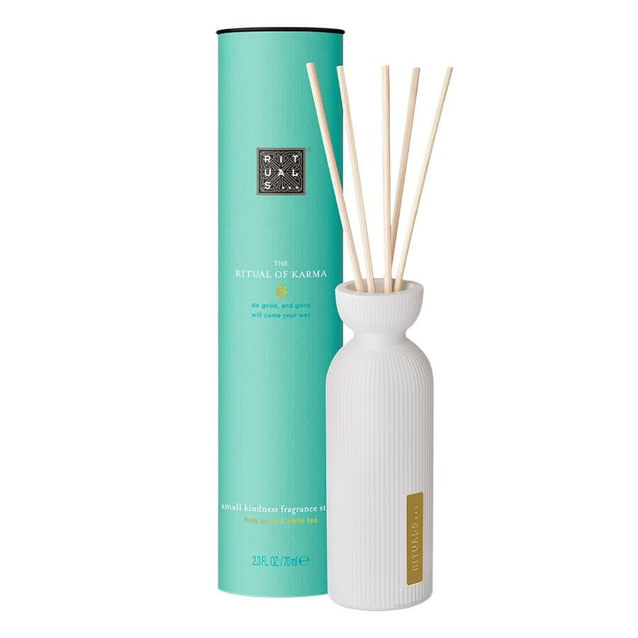 Scented sticks in a white ribbed ceramic vase, with bamboo reeds, placed beside a turquoise cylindrical box labeled "RITUALS the Ritual of Karma."