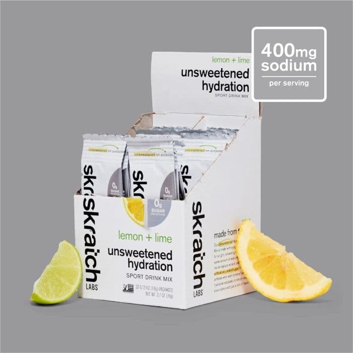 Skratch Labs Unsweetened Hydration Sport Drink Mix box featuring lemon and lime flavor, containing 20 individual packets, with fresh lemon and lime halves beside it.