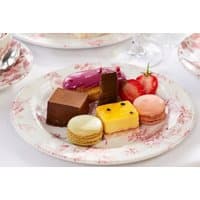 Plate with assorted desserts including macarons, chocolate squares, and a purple eclair on floral-patterned china.