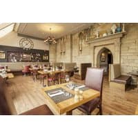 Elegant dining area with wooden tables, leather chairs, stone walls, and a large wall clock.