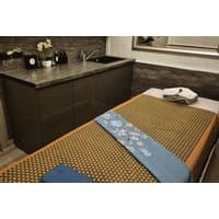 Massage table with patterned brown and blue linens in a spa room, featuring a dark wood counter and sink.