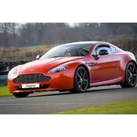 Red Aston Martin V8 Vantage sports car on a racetrack, sleek design with black alloy wheels and distinctive front grille.