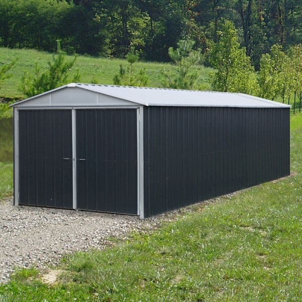 A large, dark grey metal garage with a sloped roof, double doors, and a sturdy construction, set on a gravel surface surrounded by greenery.