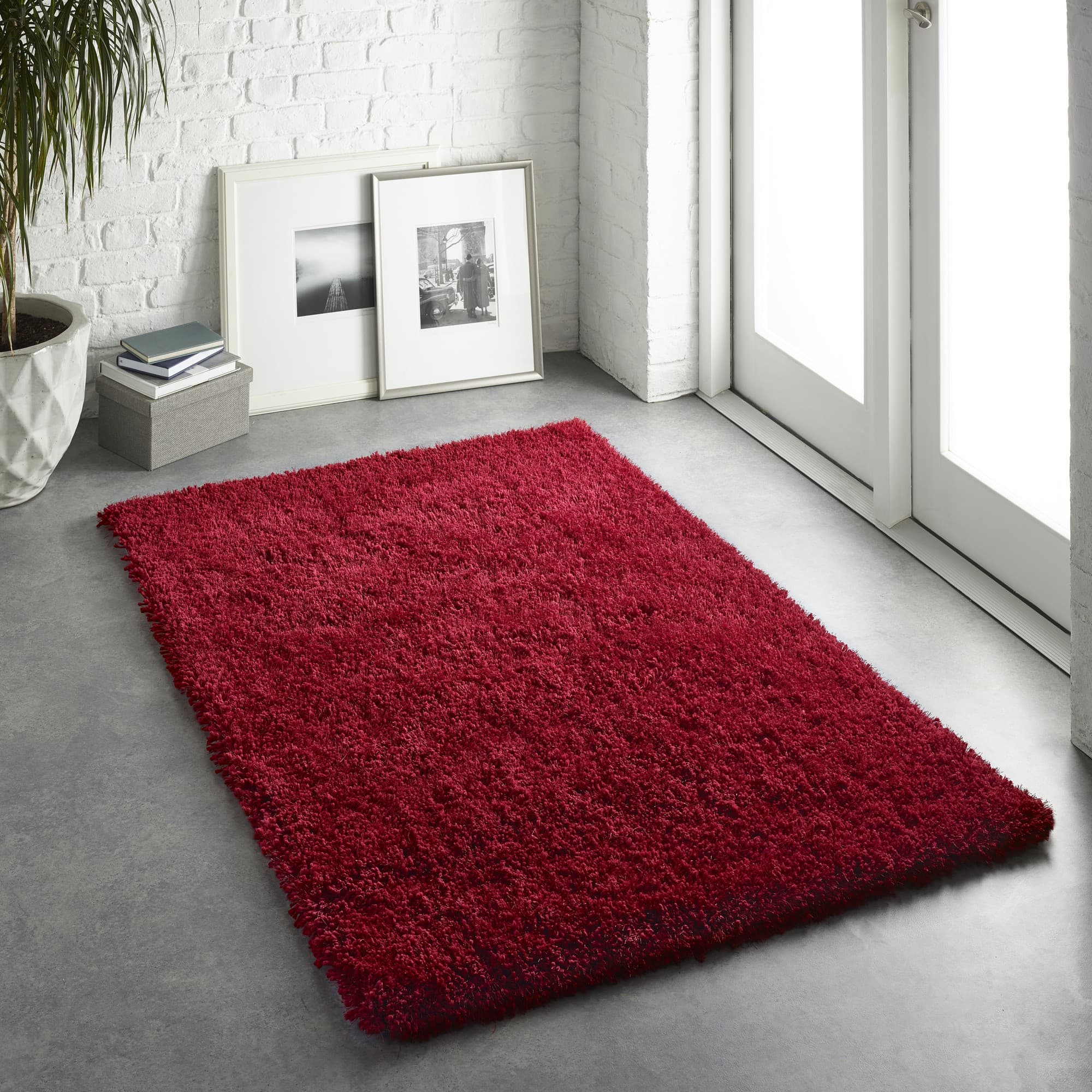 Deep red, plush shag rug measuring 110 x 160 cm, featuring a soft texture, set against a modern room with white brick walls and natural light.