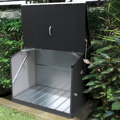 Anthracite-colored metal garden storage shed with a sloped roof, featuring a hinged lid and side door, set against lush greenery.