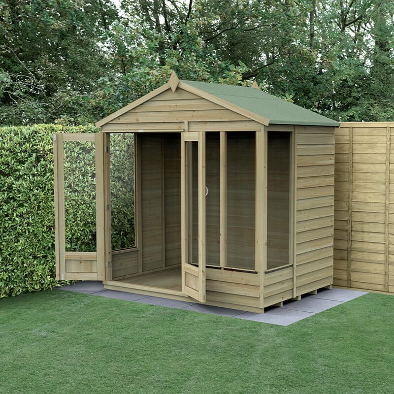 A wooden summer house with a double door, featuring a green apex roof, large windows, and a natural wood finish, set on a grassy area surrounded by hedges.