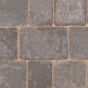Graphite-colored rumbled concrete block paving with a textured surface, featuring 134mm x 134mm x 50mm dimensions, arranged in a pattern with visible joints.