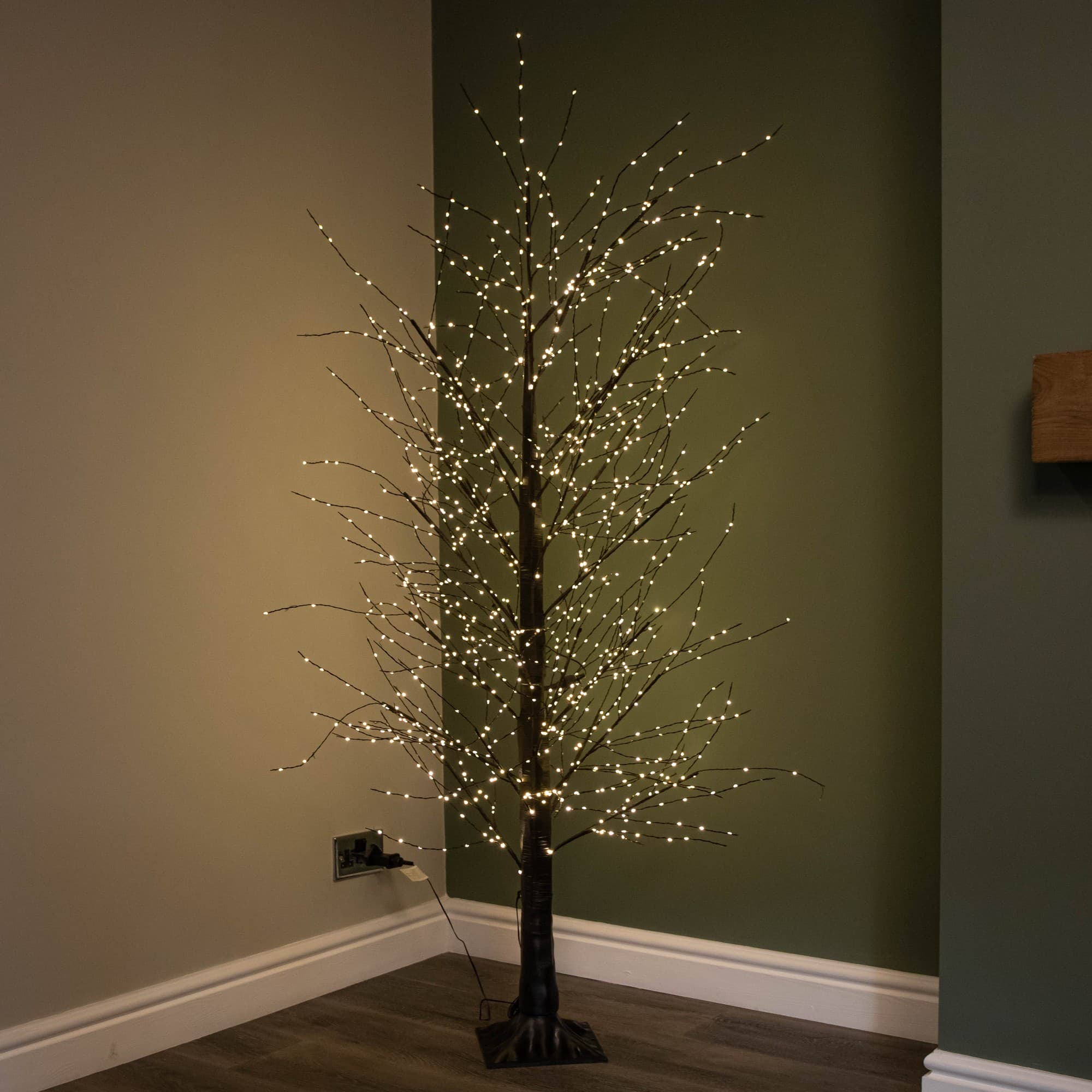 6ft black micro dot Christmas tree with 1300 warm white LEDs, featuring a slender design and twinkling lights, set against a green wall and wooden floor.