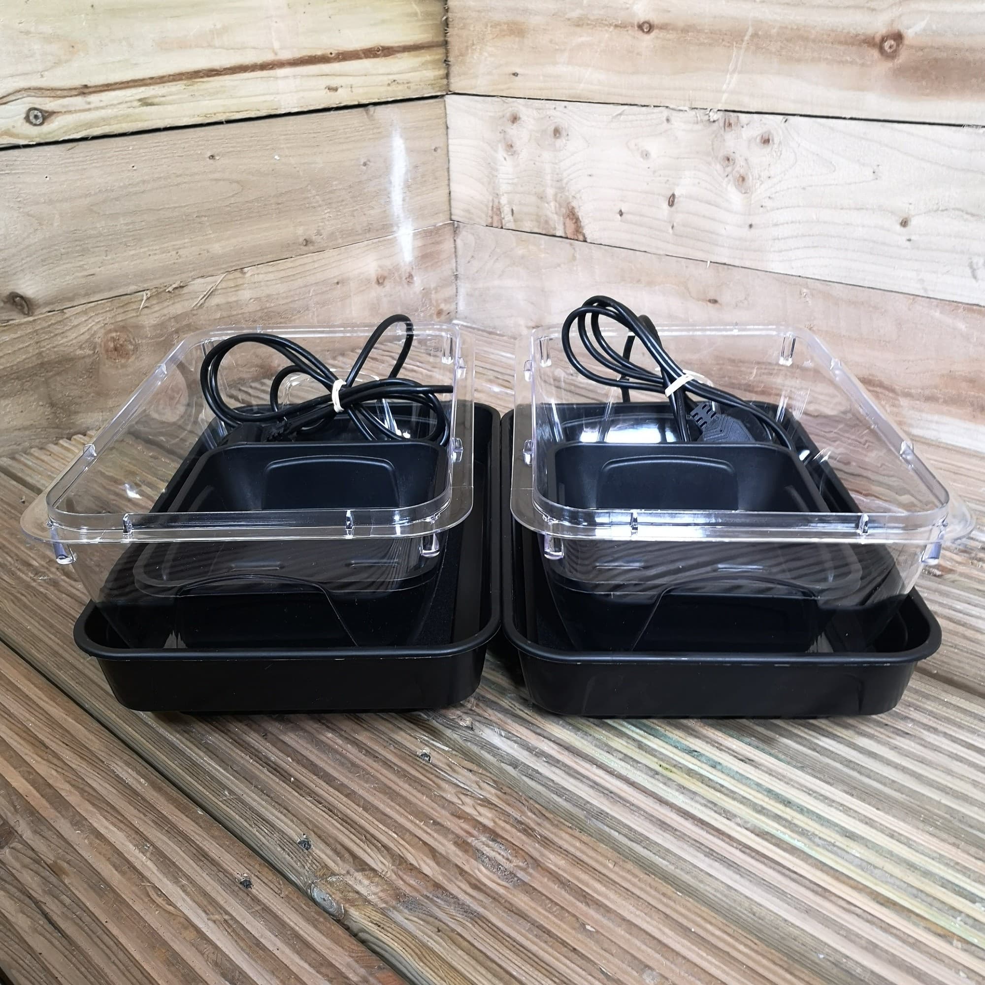 Two black heated seed starter trays with transparent plastic lids, featuring electrical cords, designed for indoor seedling planting.