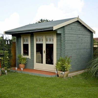 Green wooden log cabin summerhouse with a sloped roof, double doors, decorative window panes, and potted plants on a wooden deck surrounded by grass.