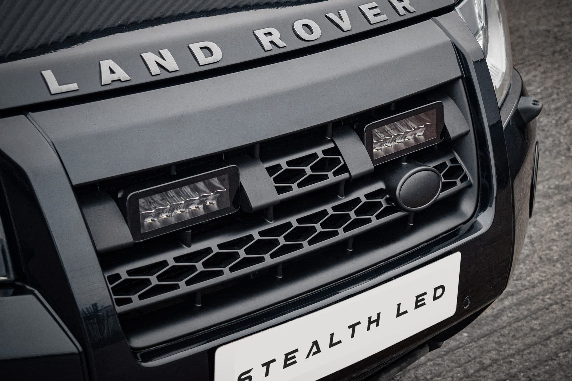 Black front grille of a Land Rover Freelander 2 featuring the "Stealth LED" logo, with two twin 7" luminous LED lights integrated into the design, showcasing a sleek, modern look.