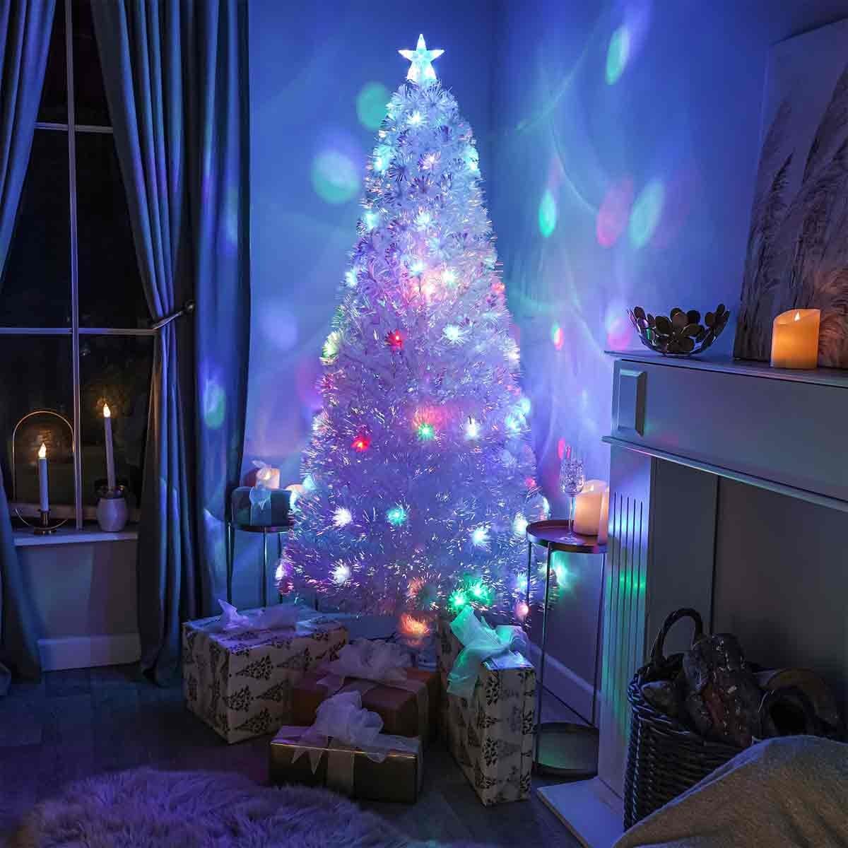 Fibre optic white Christmas tree, 7ft tall, adorned with multi-colored LED lights, set in a cozy room with wrapped gifts and soft candlelight ambiance.