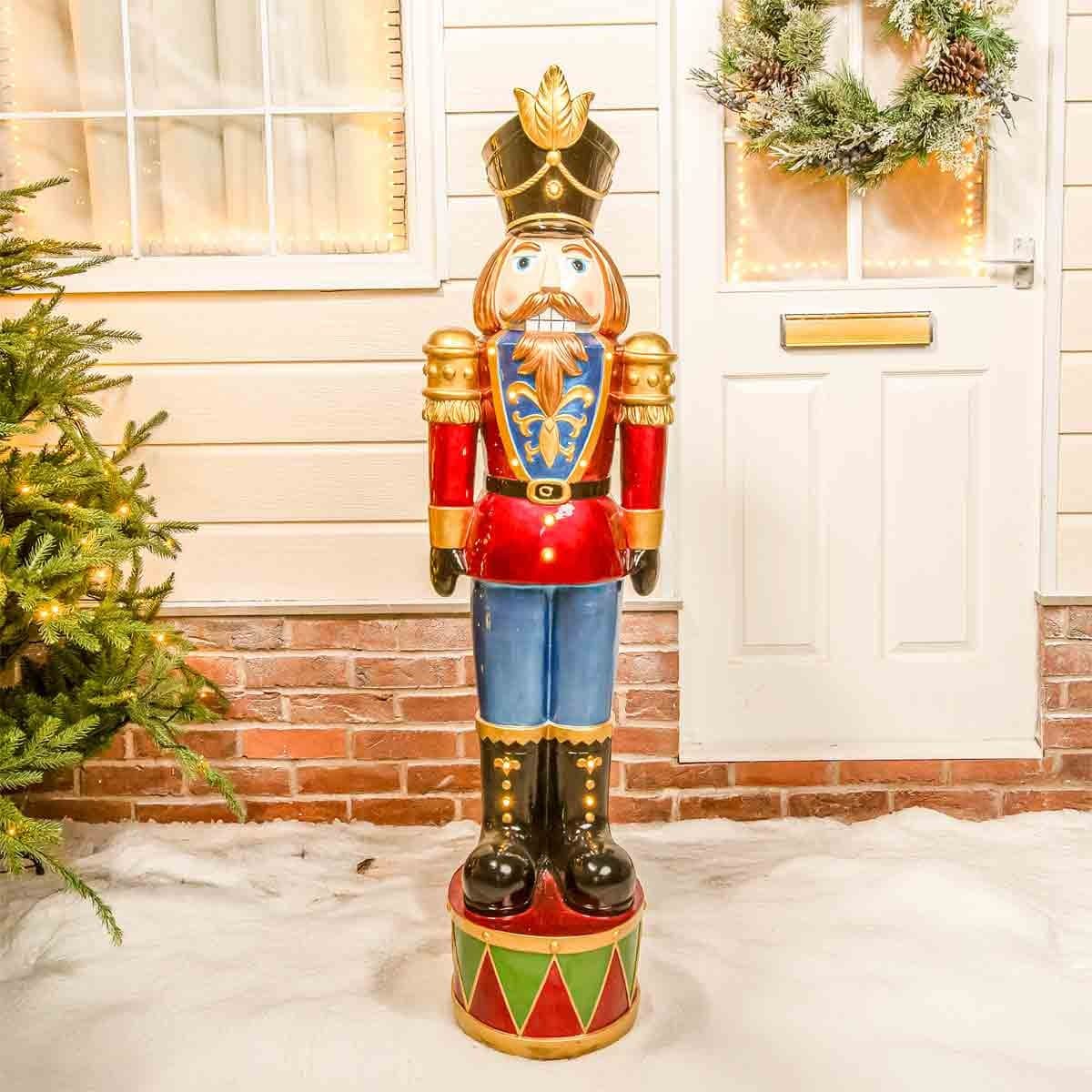 4.5ft traditional nutcracker soldier in red and blue, featuring LED lights, a gold crown, and a festive design, standing on a colorful base near a door and greenery.