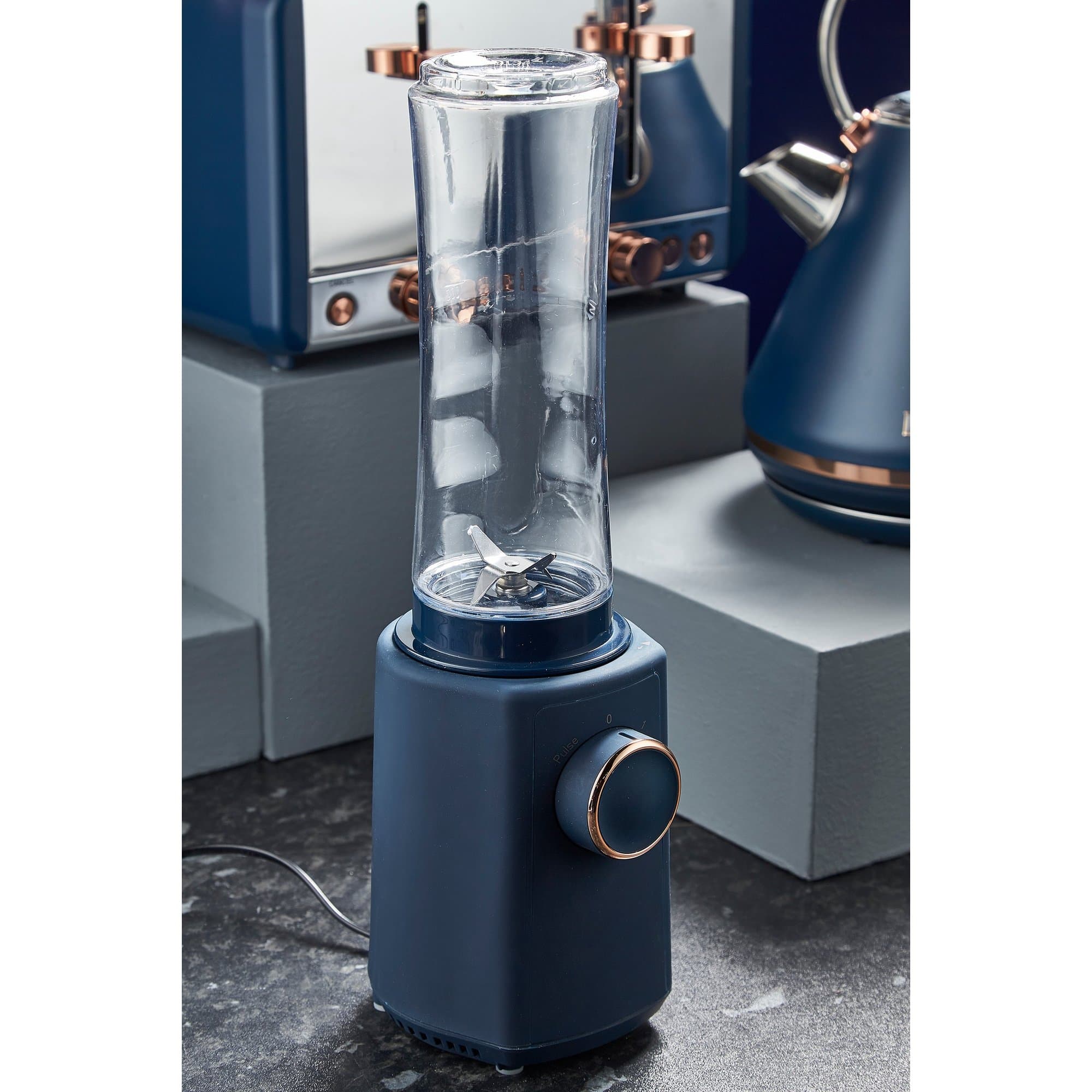 Tower Cavaletto 300W personal blender in blue with a transparent blending jar, metal base, and a copper-tone control knob, set against a gray backdrop.