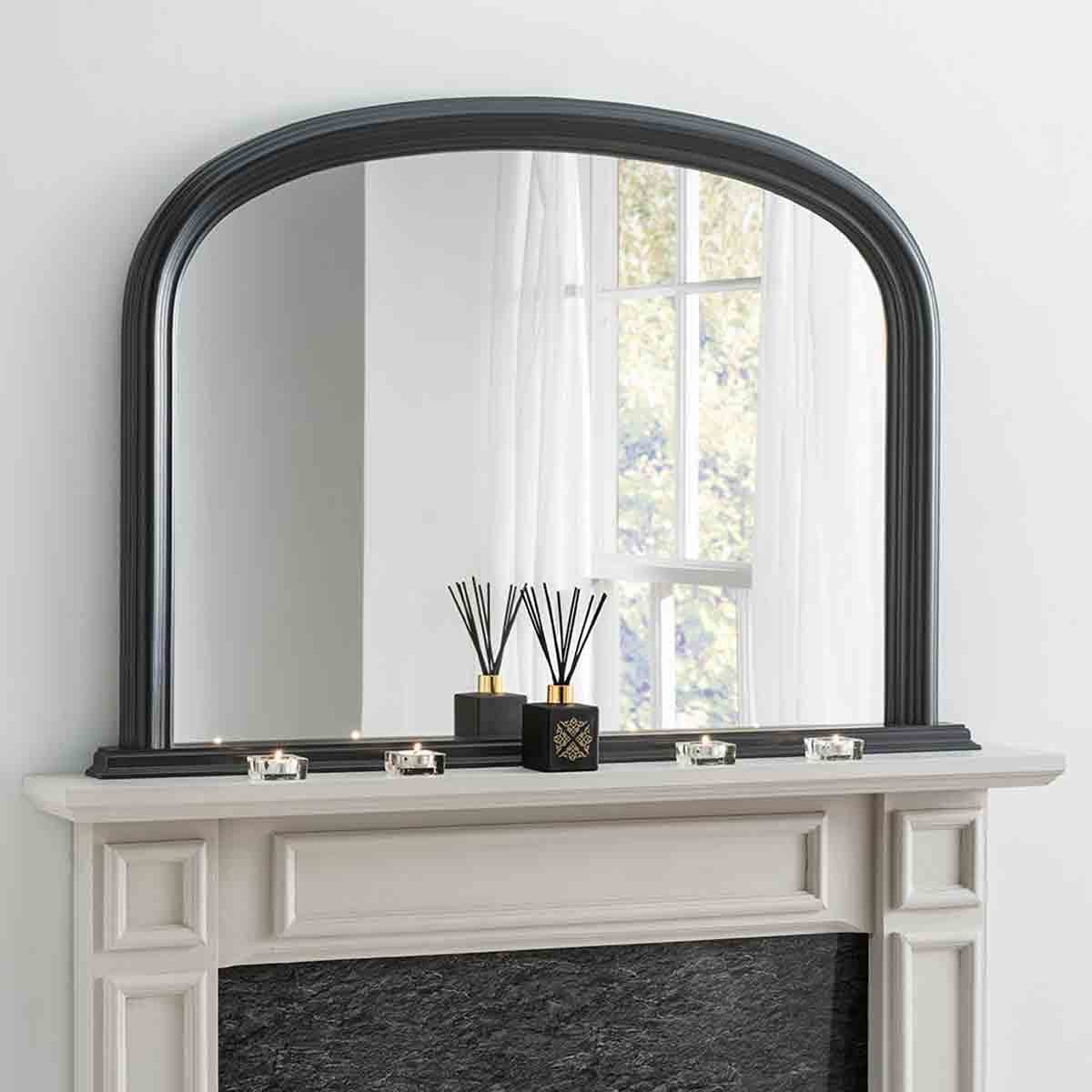 Arched contemporary black mirror with a sleek frame, measuring 112cm wide and 77cm high, displayed above a mantel with decorative candles and a diffuser.