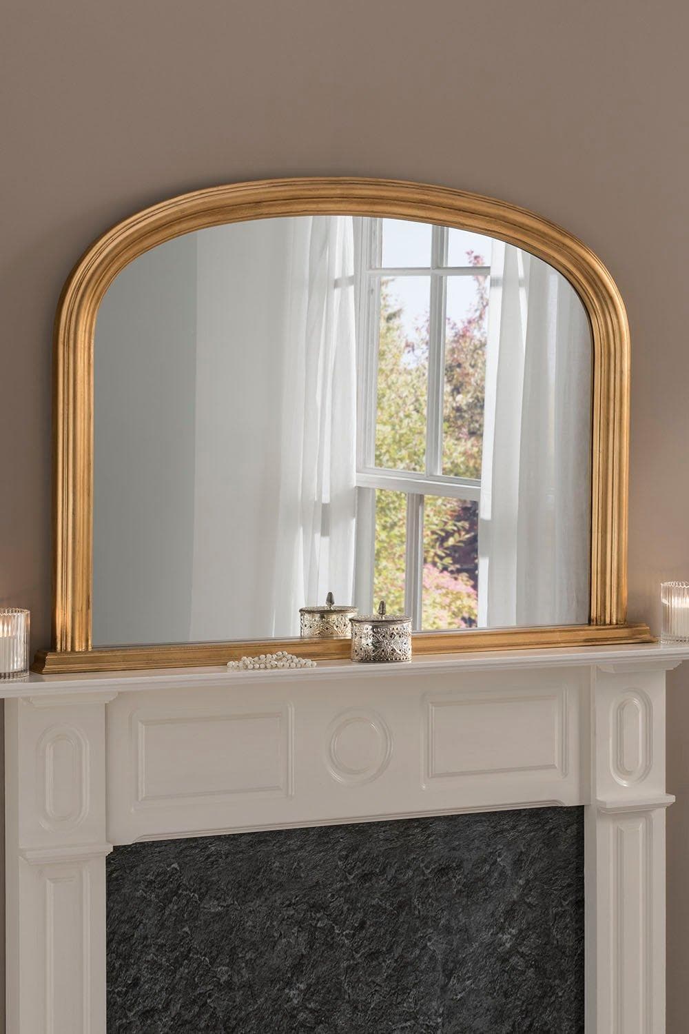 Arched contemporary mirror in metallic gold, measuring 112cm wide by 77cm high, with a sleek frame reflecting natural light and a stylish mantel below.