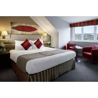 Radisson Blu Durham room with double bed, red cushions, striped bed skirt, armchairs, window view, and bedside lamps.