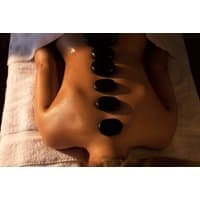 Spa treatment with hot stones on a person's back, lying on a white towel, dimly lit relaxing environment.