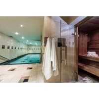 Hotel spa area with indoor pool, glass sauna, and white towels hanging on a hook.