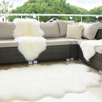 White sheepskin rug with fluffy texture draped over a wicker sofa and spread on the floor in a patio setting.