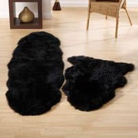 Black sheepskin double rug with a soft, fluffy texture and irregular shape on a wooden floor.