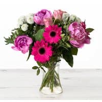 Bouquet of pink roses, peonies, gerberas, and white chrysanthemums in a clear glass vase.