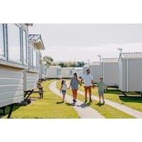 Family walking between white caravans at Flower of May Holiday Park, Yorkshire, with green lawns and clear skies.