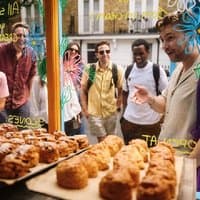 Group of people on a food tour in Notting Hill, gathered around a bakery window displaying pastries and scones.