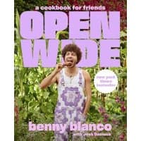 Cookbook "Open Wide" with purple text, featuring a person in floral overalls eating outdoors, surrounded by greenery.
