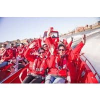 Red high-speed boat with passengers in red jackets and life vests, waving and smiling on open water.