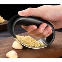 Stainless steel garlic press with black ergonomic handle, mincing garlic on a wooden board.