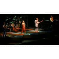 Band performing on stage with guitars, drums, and keyboards, colorful lighting highlighting musicians in dynamic poses.