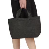 Small black felt tote bag with short handles, carried by a person wearing a black outfit.