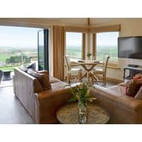 "Shooting Star" cottage interior with leather sofas, round dining table, large windows, and countryside view.