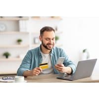 Man holding a credit card and smartphone, sitting at a desk with a laptop, representing an online financial course.