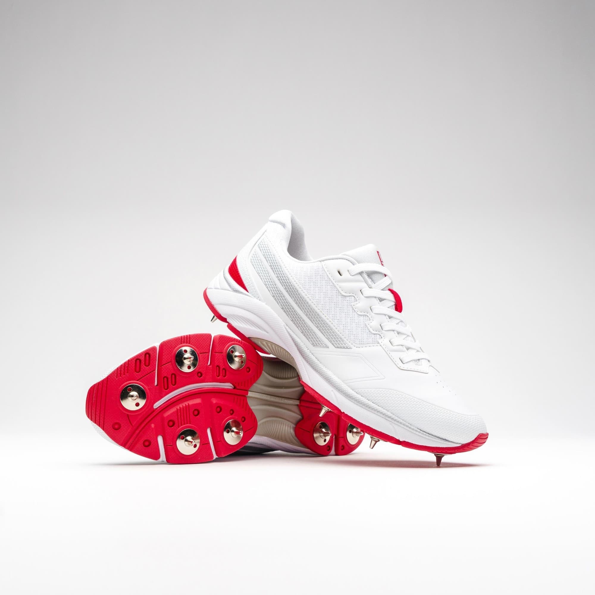 Gray-Nicolls Velocity 5.0 spike shoes in white with red accents, featuring a lightweight design, breathable mesh upper, and metallic spikes for enhanced traction on the field.