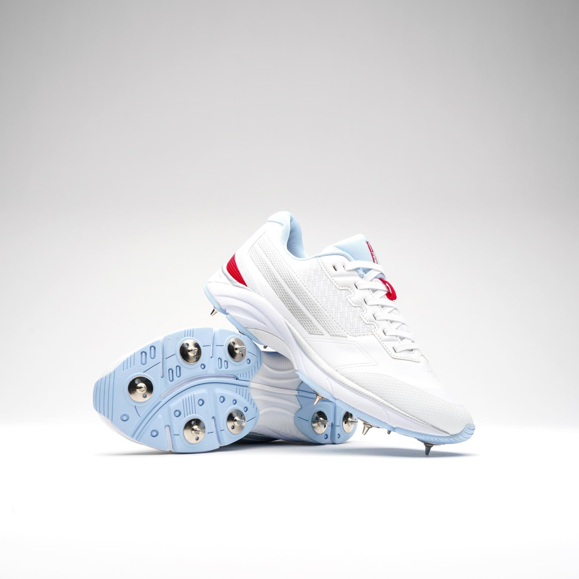 White Gray-Nicolls Velocity 5.5 spike shoes featuring a sleek design, light blue accents, and metallic spikes on the sole for enhanced traction.